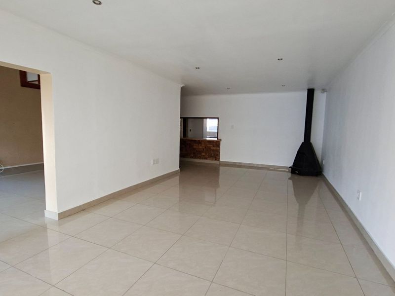 Spacious, empty living area featuring neutral tiled flooring, a modern freestanding fireplace, and a convenient pass-through window connecting to the adjacent space.