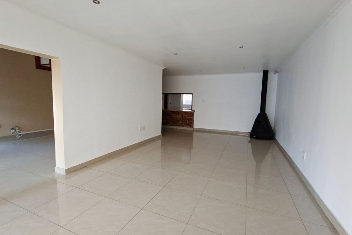 Spacious, empty living area featuring neutral tiled flooring, a modern freestanding fireplace, and a convenient pass-through window connecting to the adjacent space.