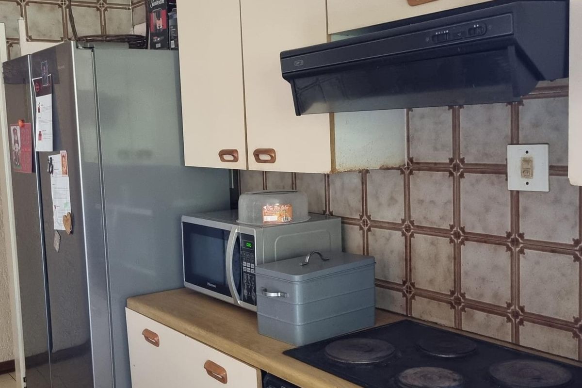 A functional kitchen featuring dated cabinetry, a built-in electric hob, an extractor fan, and tiled splashbacks.
