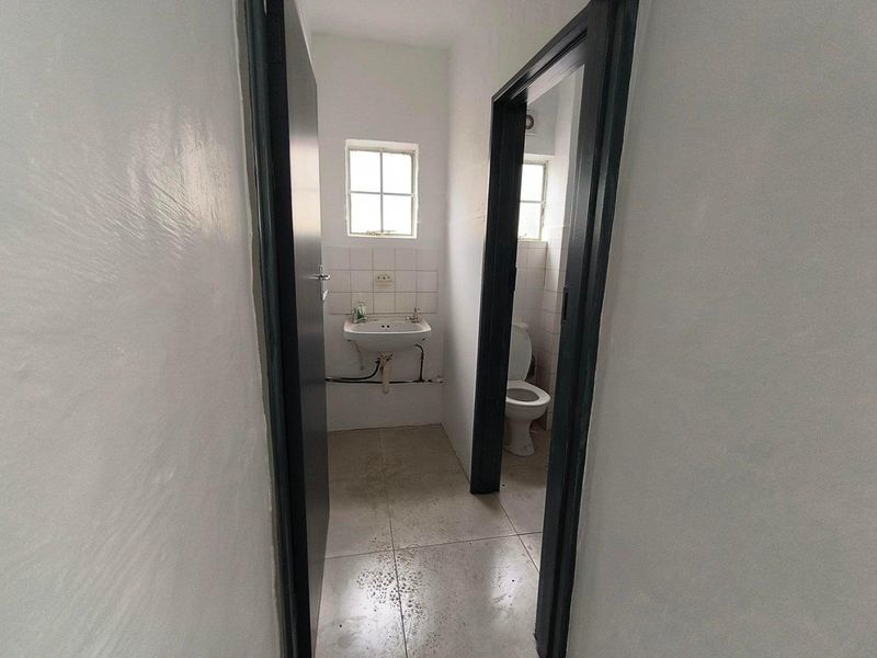 A functional bathroom space featuring a wall-mounted basin, toilet, and tiled flooring, requiring cosmetic updates to improve its overall condition.
