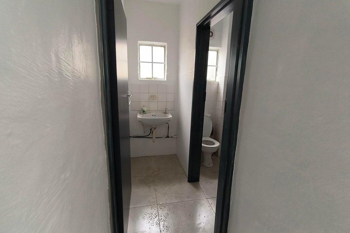 A functional bathroom space featuring a wall-mounted basin, toilet, and tiled flooring, requiring cosmetic updates to improve its overall condition.