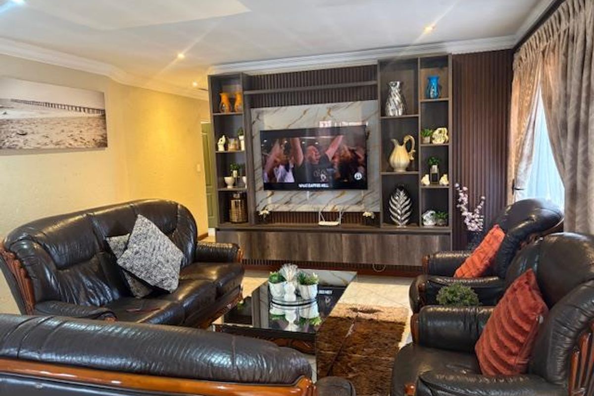 A well-maintained living room featuring custom built-in cabinetry with integrated shelving and recessed lighting, complemented by tiled flooring and coved cornicing.