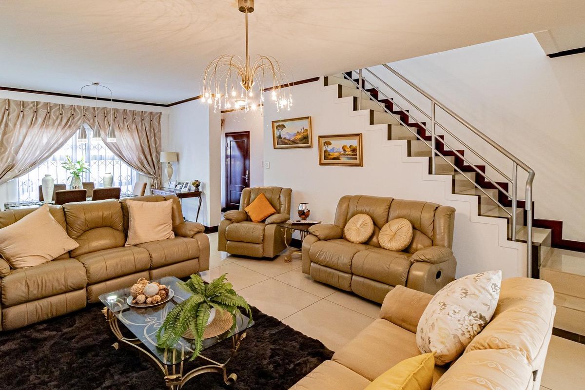 Spacious open-plan living area featuring tiled flooring, a modern staircase with stainless steel balustrades, and elegant lighting fixtures.
