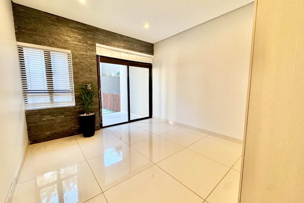 A bright, empty living area featuring large format porcelain tiles, a textured stone feature wall, and sliding glass doors leading to an outdoor space.