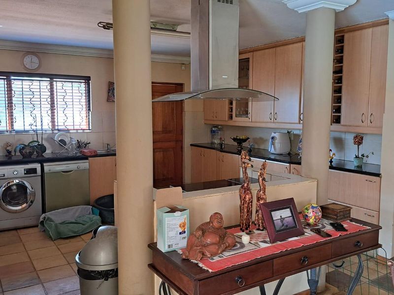 A functional kitchen featuring light wood cabinetry, dark countertops, a central extractor fan, and tiled flooring, separated from the living area by structural columns.