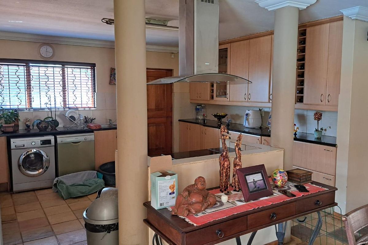A functional kitchen featuring light wood cabinetry, dark countertops, a central extractor fan, and tiled flooring, separated from the living area by structural columns.