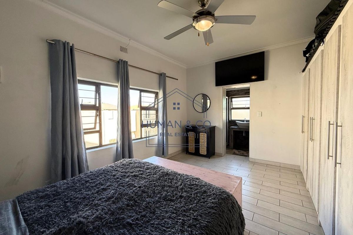 A bedroom featuring tiled flooring, built-in cupboards, a ceiling fan, and an en-suite bathroom access.