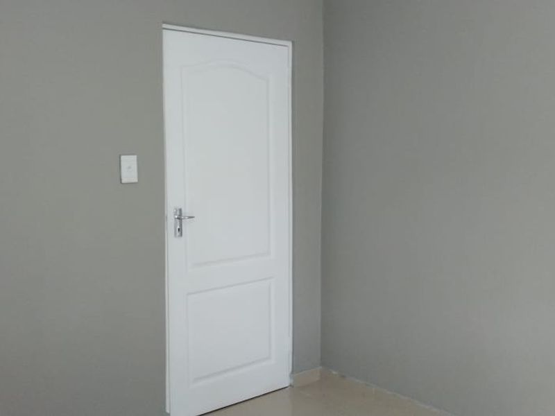 A simple, empty bedroom interior featuring neutral grey walls and a white panelled door.