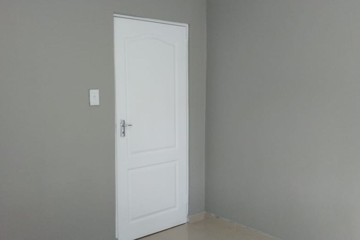 A simple, empty bedroom interior featuring neutral grey walls and a white panelled door.