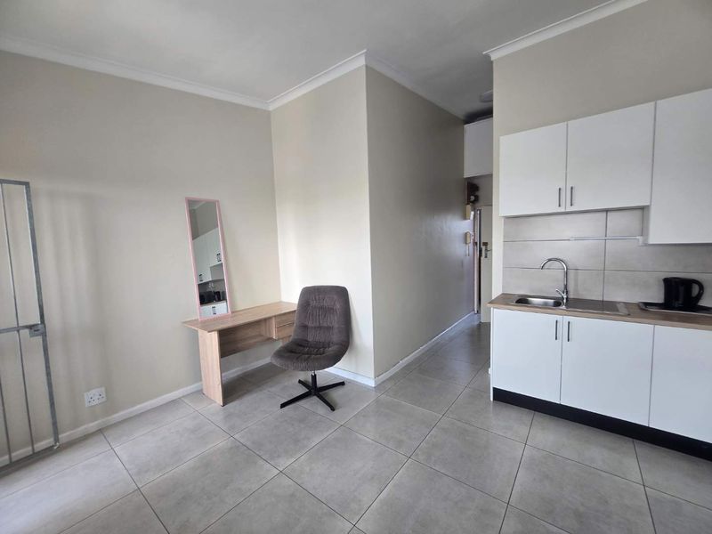 Open plan living area featuring tiled flooring and a compact kitchen with white cabinetry and stainless steel sink.