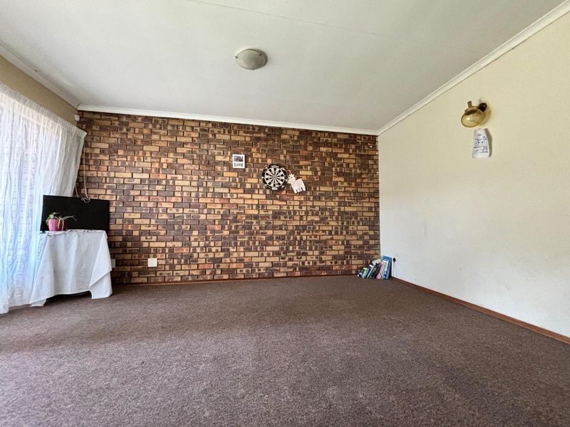 A living room featuring an exposed brick accent wall, carpeted flooring, and neutral wall finishes, offering a blank canvas for interior design updates.
