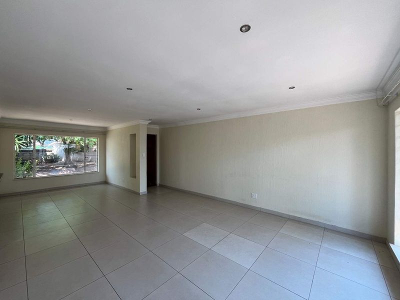 A spacious, empty living area featuring neutral tiled flooring, recessed downlighting, and a built-in wall niche, offering a blank canvas for interior design.