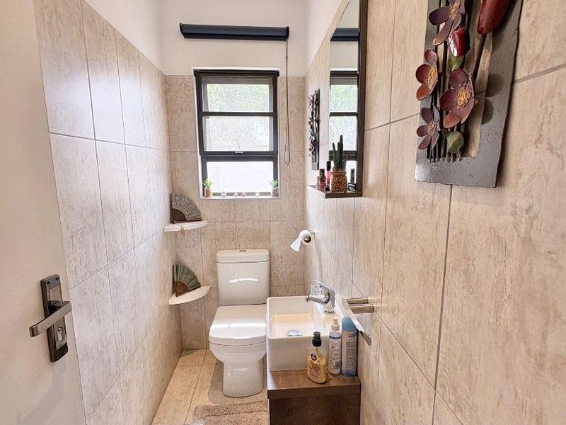 A compact guest bathroom featuring floor-to-ceiling neutral tiling, a wall-mounted vanity with a basin, and a modern toilet.