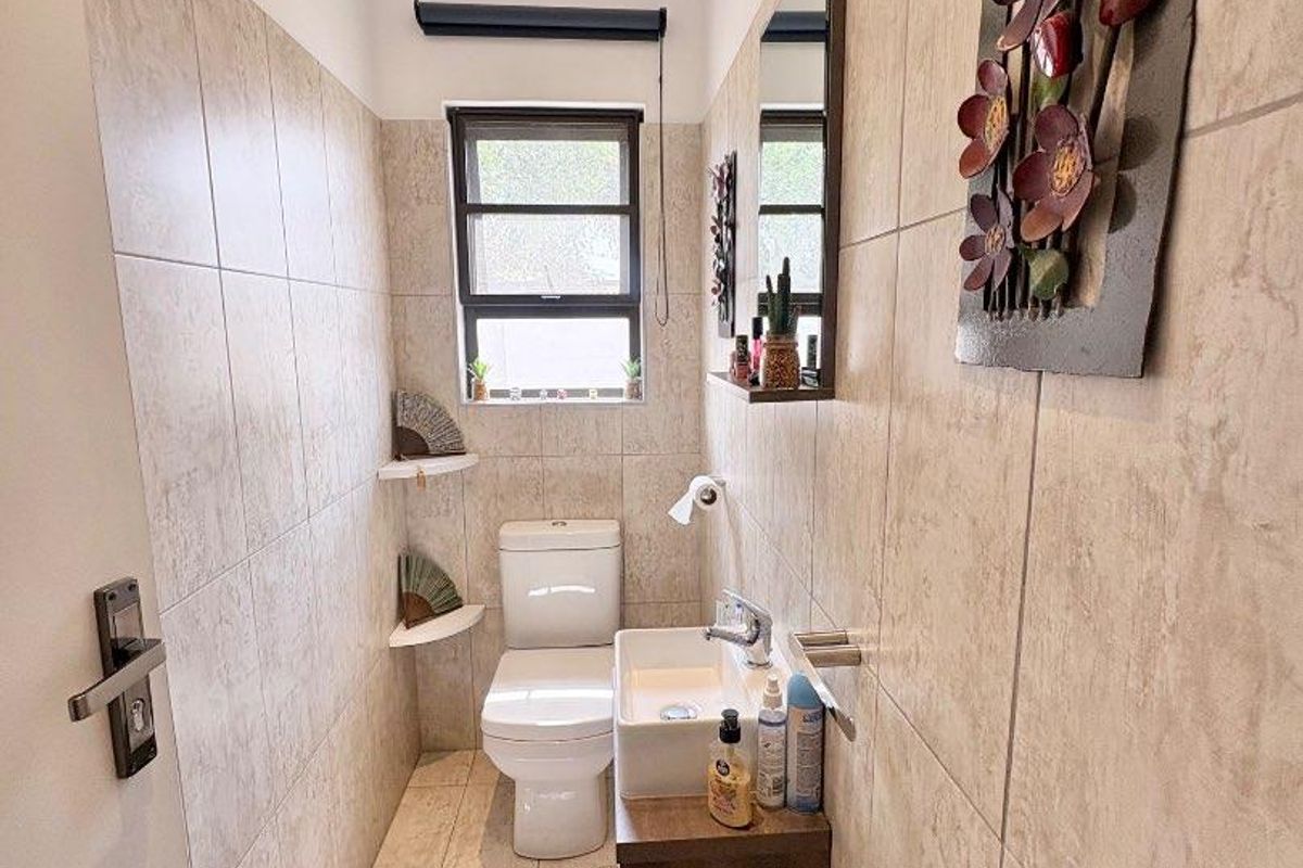 A compact guest bathroom featuring floor-to-ceiling neutral tiling, a wall-mounted vanity with a basin, and a modern toilet.