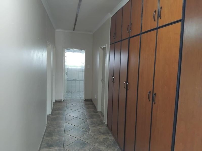 A functional hallway featuring extensive built-in wooden cabinetry for storage and durable tiled flooring, leading towards a bathroom area.