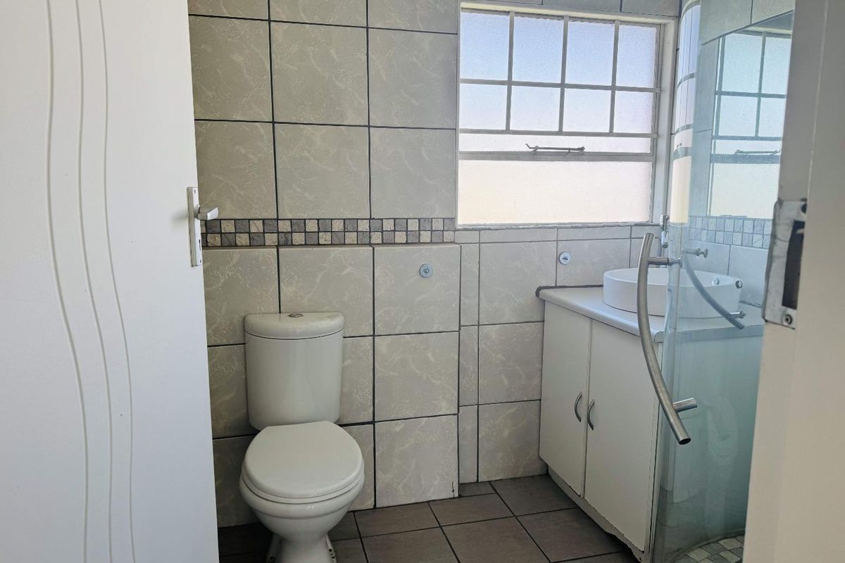 A functional bathroom featuring a toilet, vanity with vessel sink, and a glass-enclosed shower, finished with neutral wall and floor tiling.