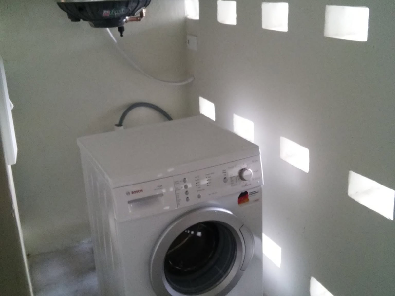 A functional laundry area featuring a wall-mounted electric water heater and decorative ventilation blocks.