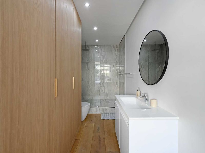 Modern bathroom featuring a sleek vanity, timber flooring, built-in cabinetry, and a spacious walk-in shower with contemporary tiled finishes.