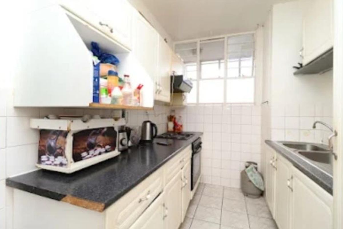 A compact galley-style kitchen featuring white cabinetry, tiled splashbacks, a dark laminate countertop, and a built-in oven with a gas hob.