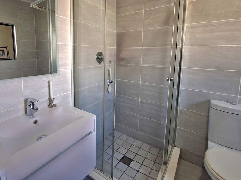 A modern bathroom featuring a glass-enclosed shower, a wall-mounted vanity with a basin, and neutral tiled finishes throughout.