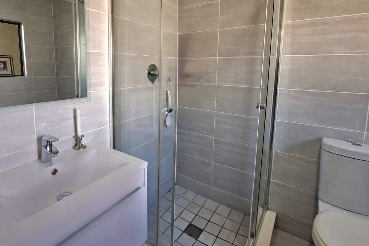 A modern bathroom featuring a glass-enclosed shower, a wall-mounted vanity with a basin, and neutral tiled finishes throughout.