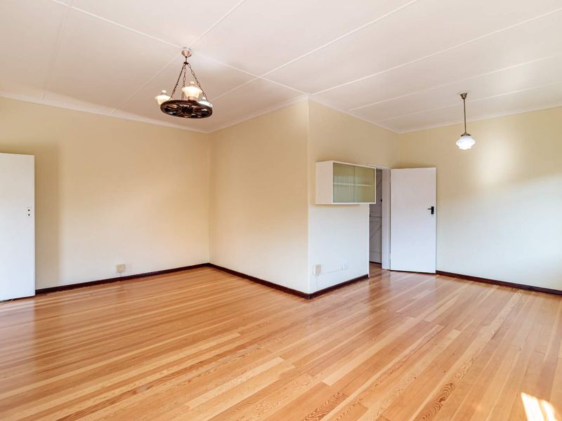 A spacious, empty living area featuring polished timber flooring, neutral walls, and built-in cabinetry, offering a versatile blank canvas for interior design.