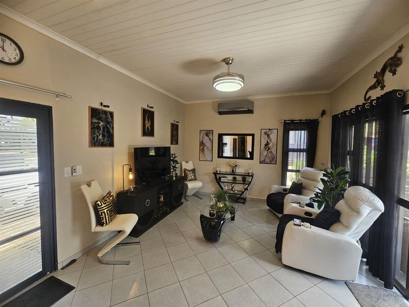 A well-maintained living room featuring tiled flooring, a ceiling fan, and a split-system air conditioner, providing a comfortable and functional living space.