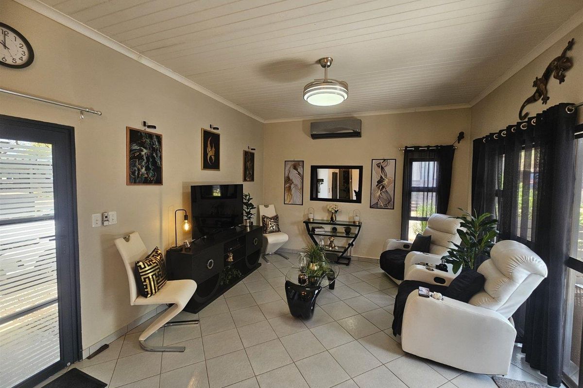 A well-maintained living room featuring tiled flooring, a ceiling fan, and a split-system air conditioner, providing a comfortable and functional living space.