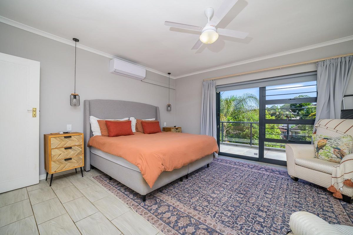 Spacious bedroom featuring a ceiling fan, wall-mounted air conditioning unit, and large sliding glass doors opening onto a private balcony.