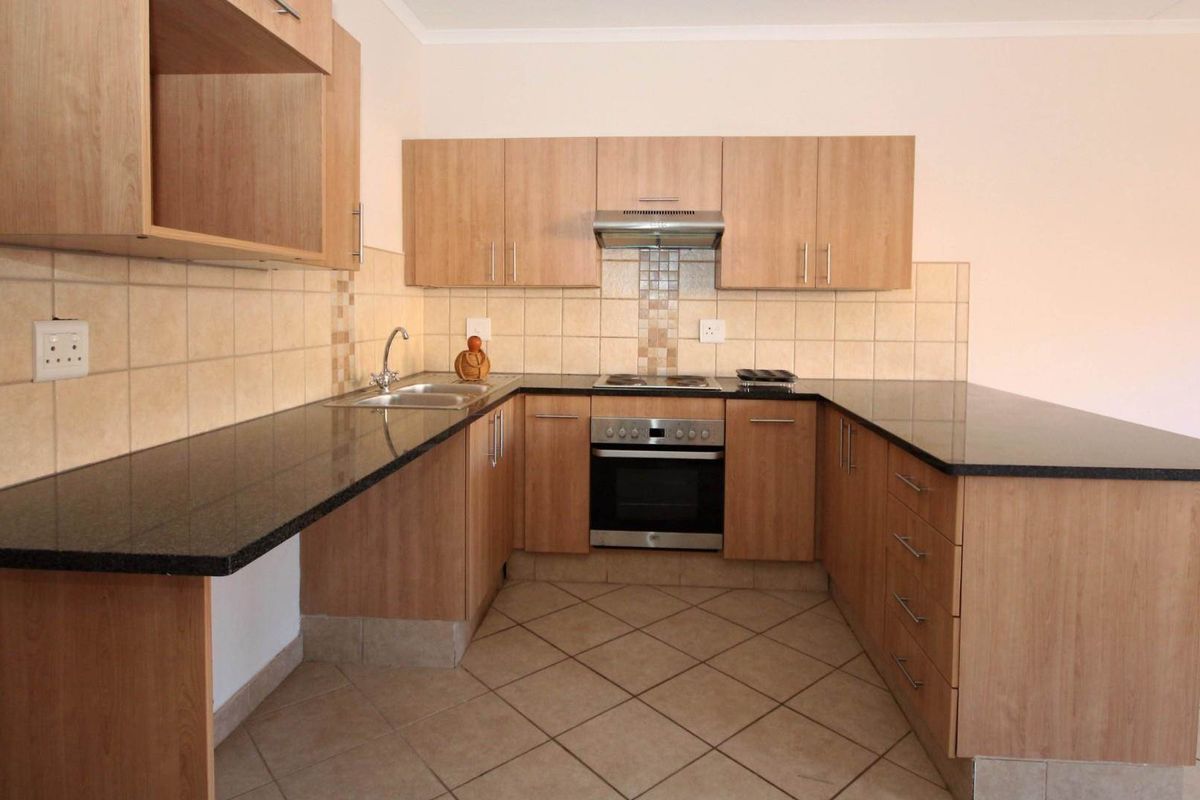 A functional U-shaped kitchen featuring light wood-finish cabinetry, dark granite countertops, built-in oven, hob, and extractor fan with neutral tiled flooring.