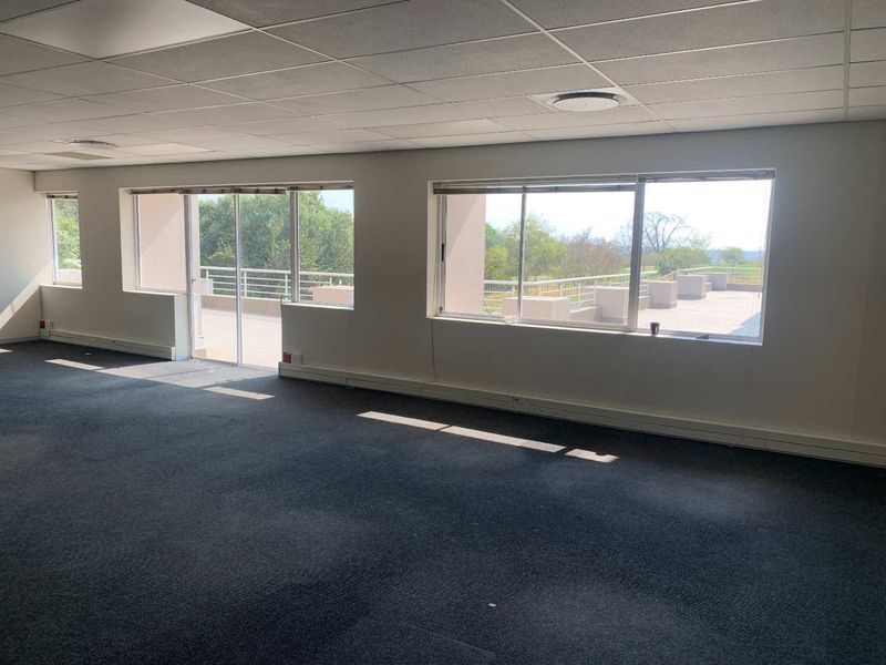 Spacious open-plan office area featuring large windows, carpeted flooring, and direct access to an outdoor balcony area.