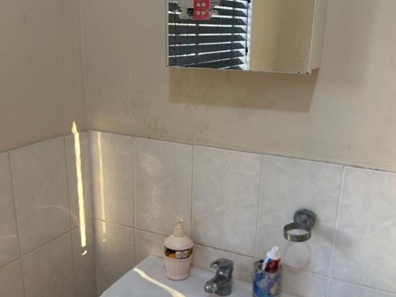 A compact bathroom vanity area featuring a wall-mounted basin, mixer tap, and a mirrored medicine cabinet with tiled splashback.