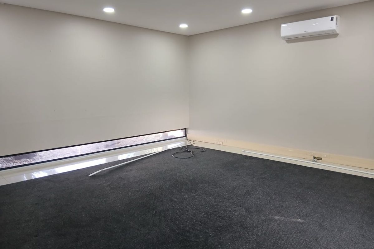 A clean, empty office space featuring dark carpeting, recessed ceiling lighting, a split-system air conditioner, and a low-profile horizontal window.