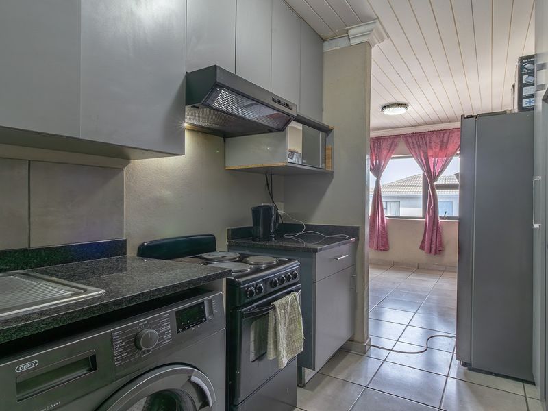 Compact kitchen featuring grey cabinetry, granite countertops, and a built-in extractor fan, with tiled flooring and an adjacent living area.