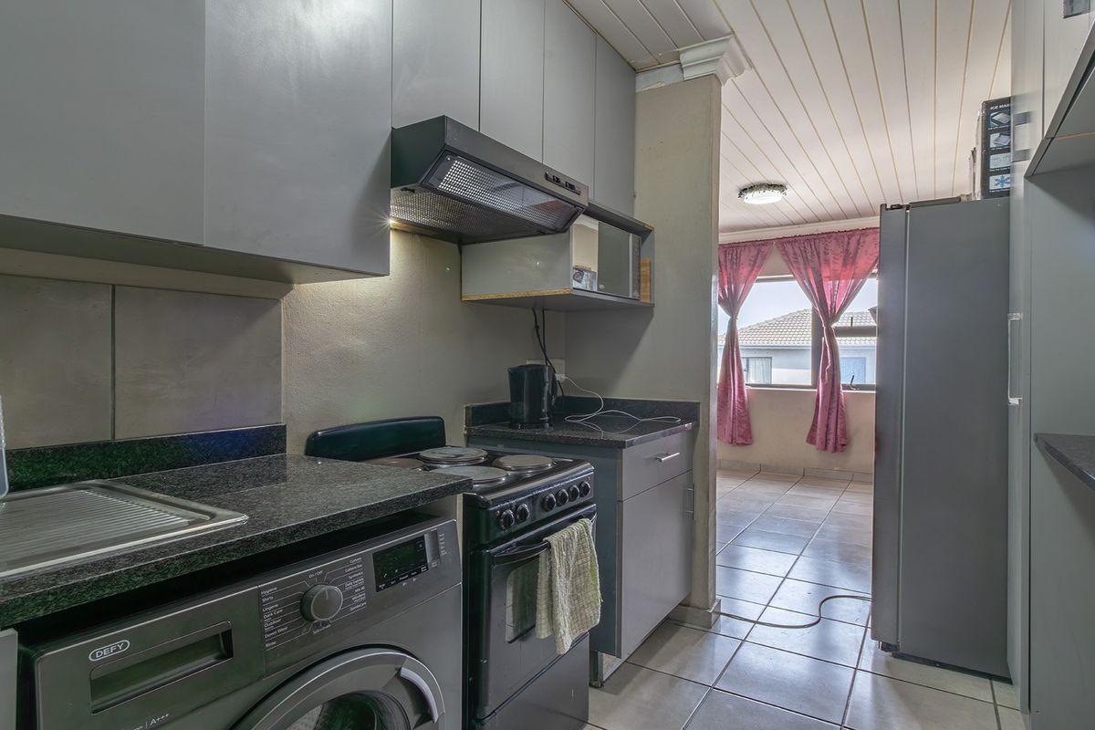 Compact kitchen featuring grey cabinetry, granite countertops, and a built-in extractor fan, with tiled flooring and an adjacent living area.