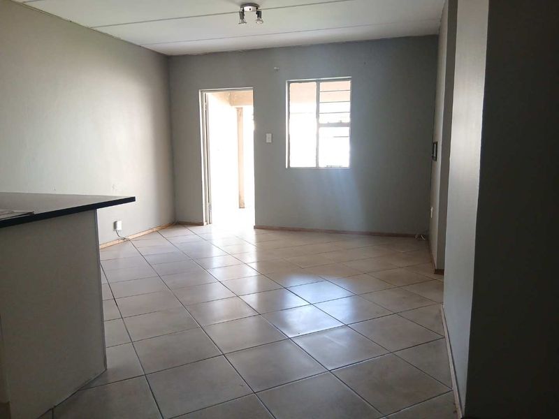 An empty open-plan living area featuring tiled flooring and a breakfast counter, providing a blank canvas for potential interior design and renovation.