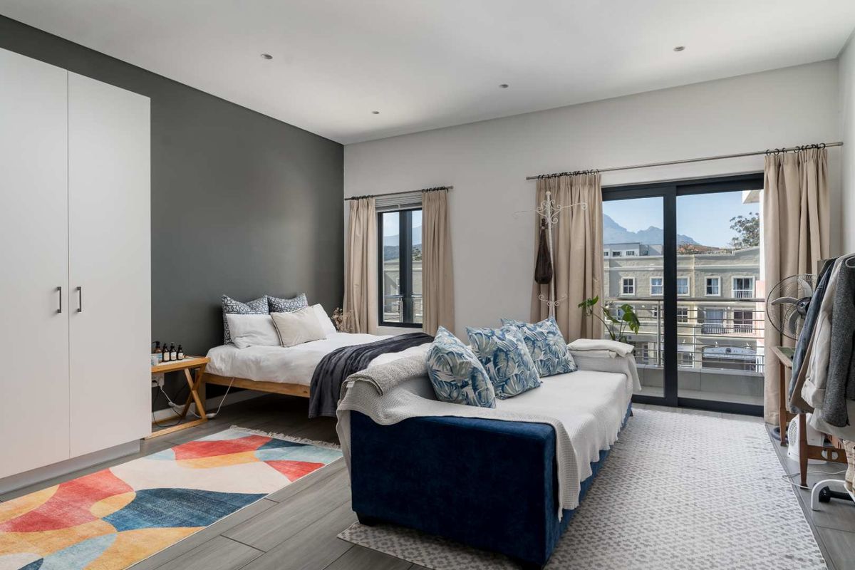 A well-lit bedroom featuring built-in wardrobes, recessed ceiling lighting, and sliding glass doors that open onto a private balcony with mountain views.