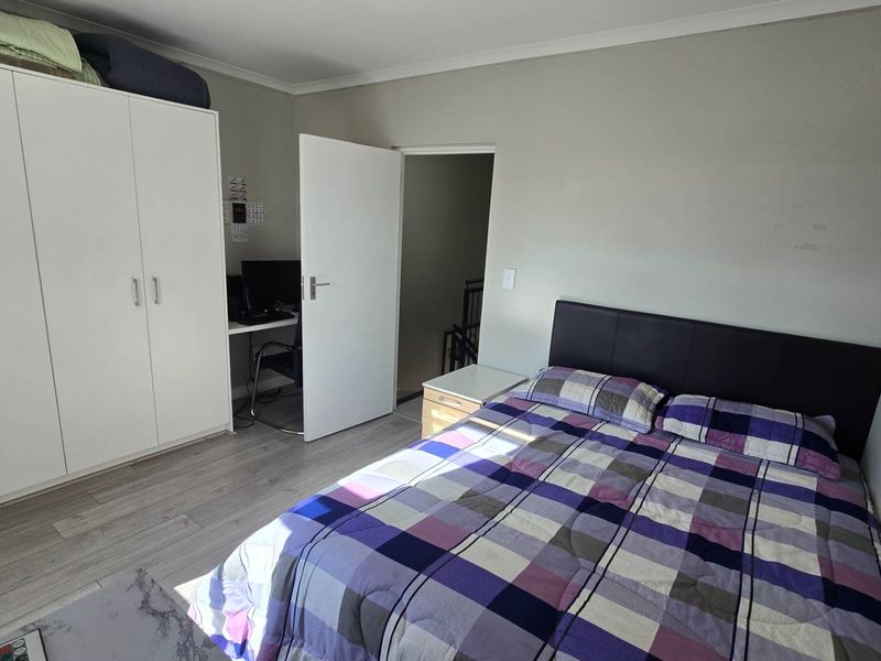 A functional bedroom featuring laminate flooring, a built-in wardrobe, and direct access to an adjacent hallway.