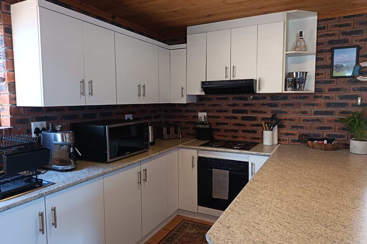 A functional kitchen featuring white cabinetry, granite-look countertops, exposed brick walls, and a timber ceiling, offering a rustic yet modern aesthetic.