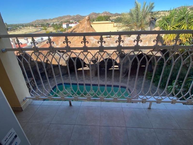 A balcony with tiled flooring and a decorative wrought iron railing, offering an elevated view of the swimming pool and surrounding landscape.