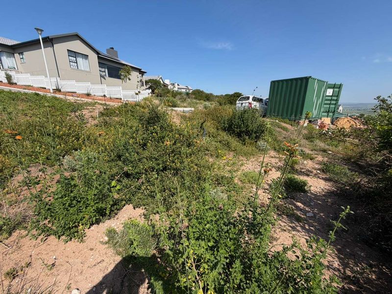 A sloped vacant residential plot featuring natural vegetation, with neighboring properties visible in the background.