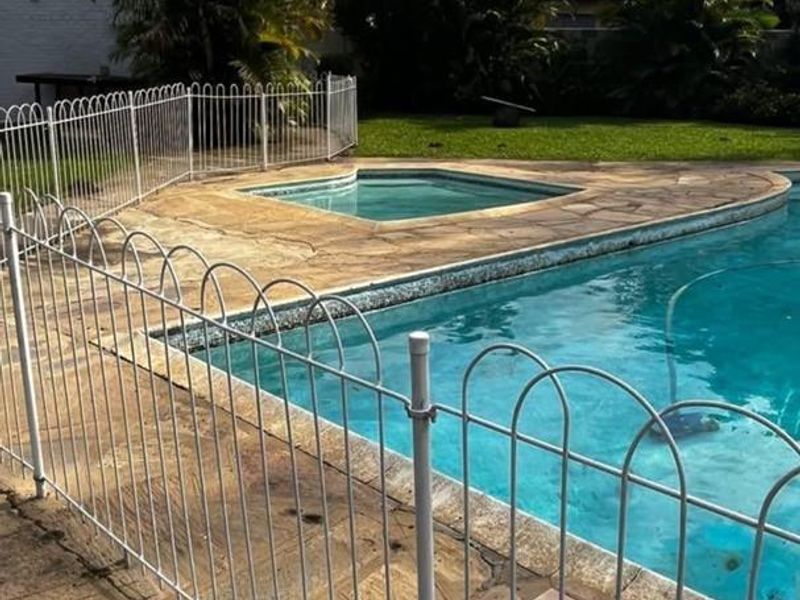 Outdoor pool area featuring a swimming pool, integrated spa, and metal safety fencing set within a paved garden space.