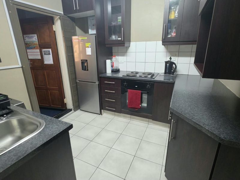 A functional kitchen featuring dark wood cabinetry, laminate countertops, a built-in oven with electric hob, and tiled flooring.
