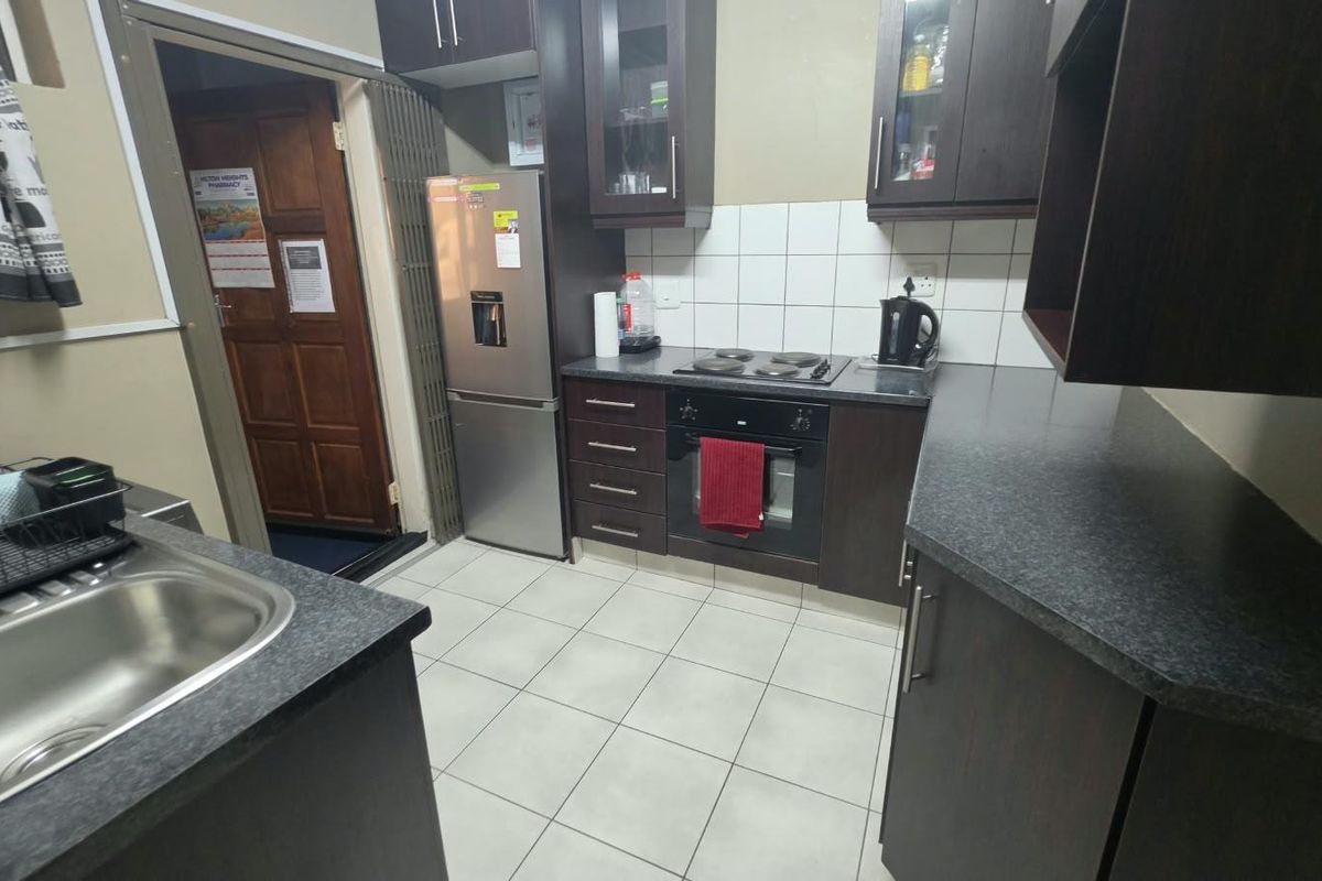 A functional kitchen featuring dark wood cabinetry, laminate countertops, a built-in oven with electric hob, and tiled flooring.