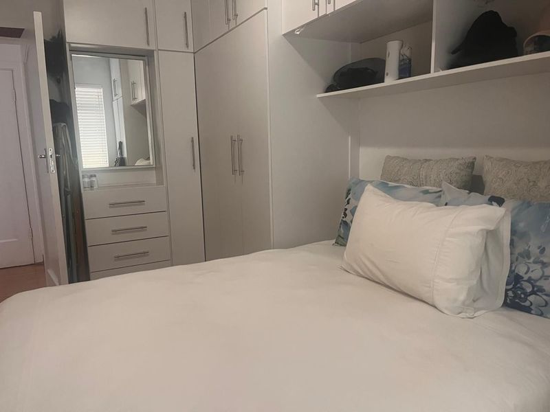 A well-organized bedroom featuring extensive built-in cabinetry, integrated storage drawers, and a vanity mirror, maximizing space efficiency.