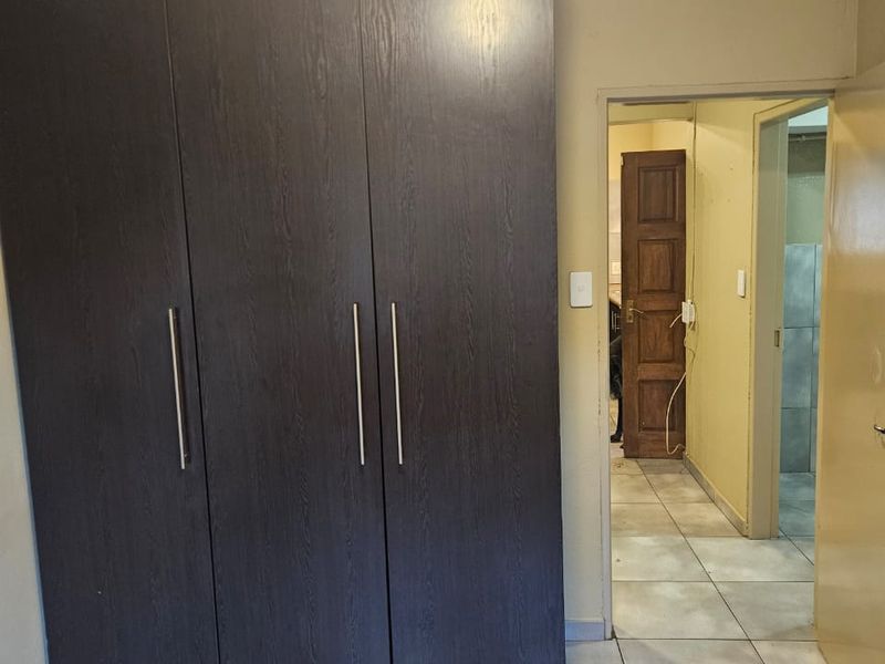 A bedroom featuring a large dark wood built-in wardrobe, tiled flooring, and coving, with a view through to an adjacent hallway and bathroom.