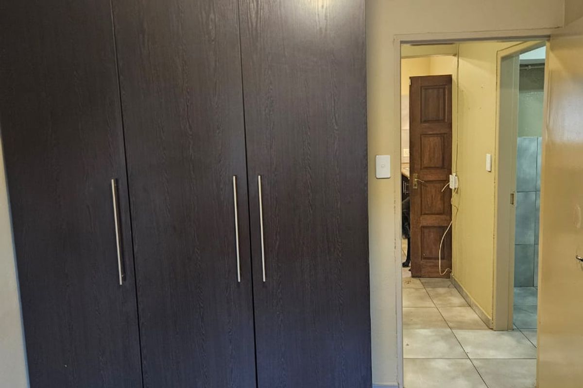 A bedroom featuring a large dark wood built-in wardrobe, tiled flooring, and coving, with a view through to an adjacent hallway and bathroom.