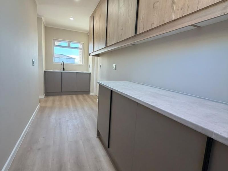A modern, clean scullery featuring extensive built-in cabinetry, laminate countertops, and a sleek under-mount sink, providing ample storage and prep space.