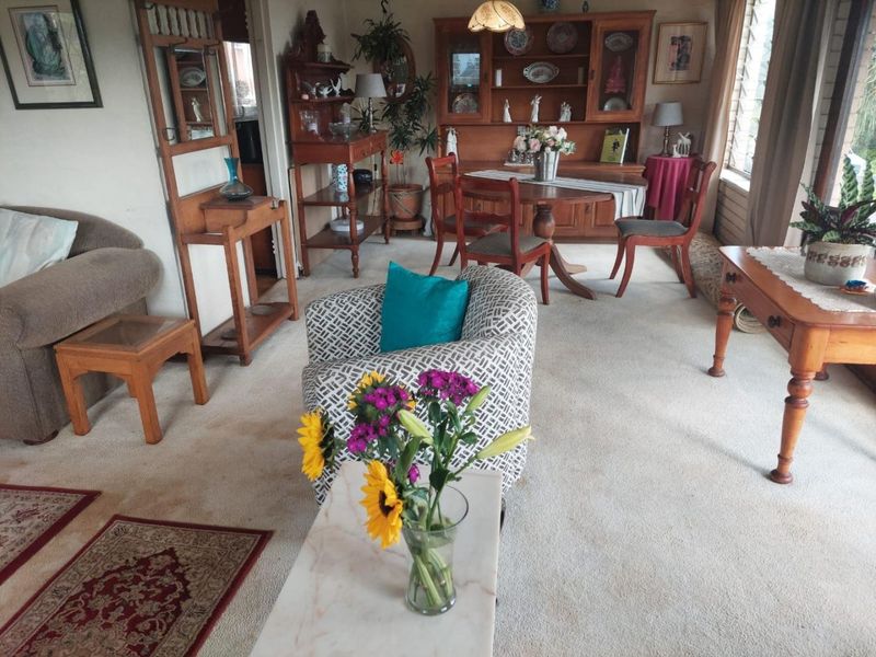 A traditional living and dining area featuring carpeted flooring and large louvre windows, offering a classic, lived-in aesthetic.