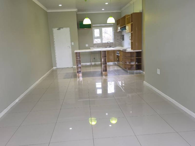 A bright, open-plan living and kitchen area featuring modern tiled flooring, recessed lighting, and a functional kitchen island with built-in cabinetry.